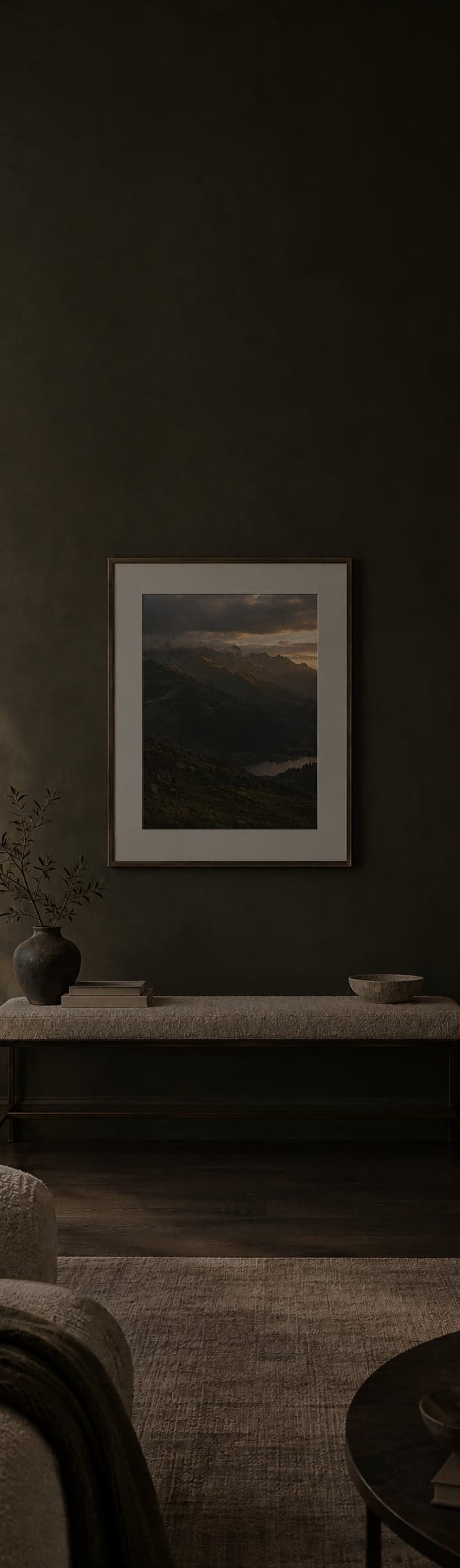A framed mountain print with a white mat on a dark olive wall above a low bench