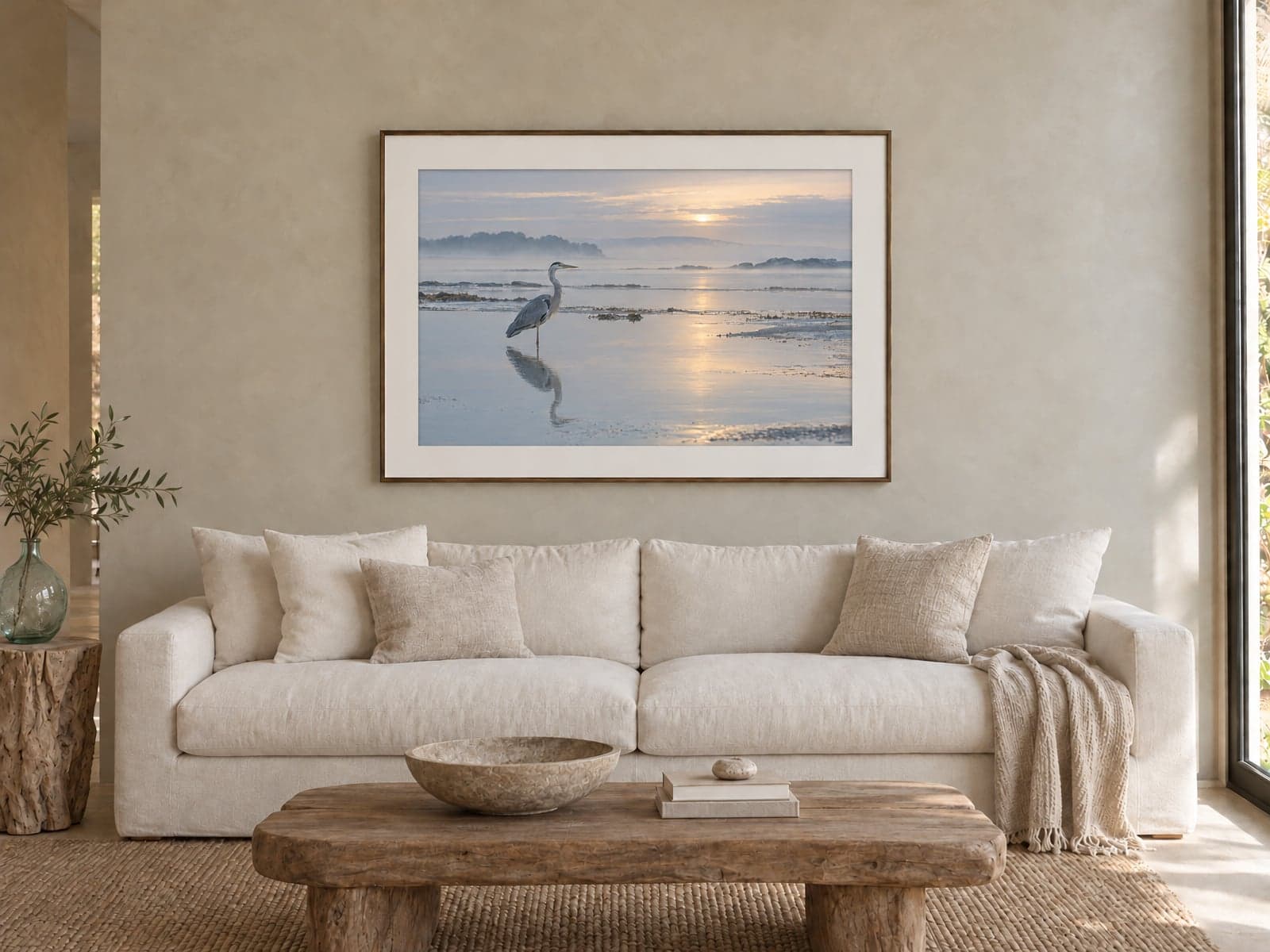 A framed print of a heron at sunrise above a white sofa