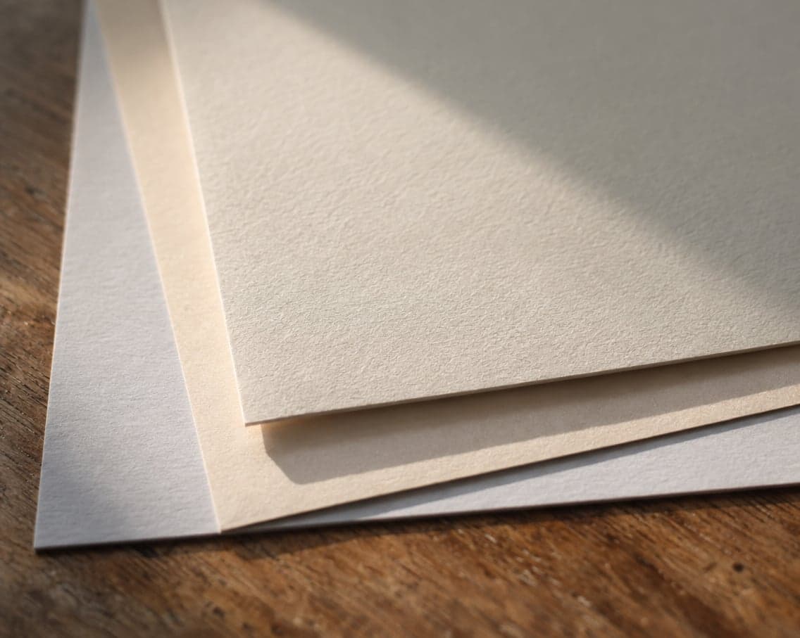 Three sheets of fine art paper in different whites, overlapping on a wooden table