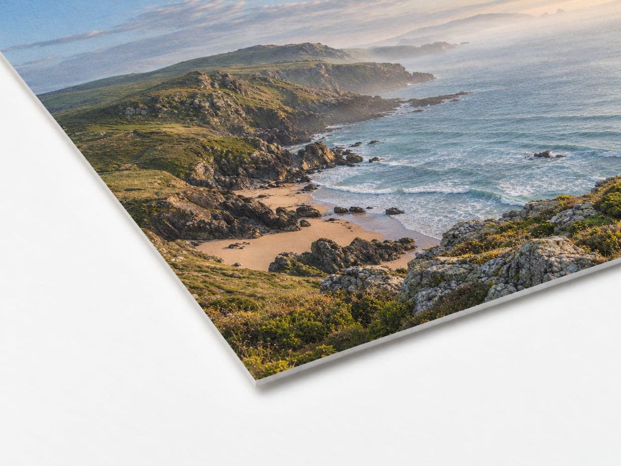 The corner of a cotton rag print of a green coastline and a sandy cove