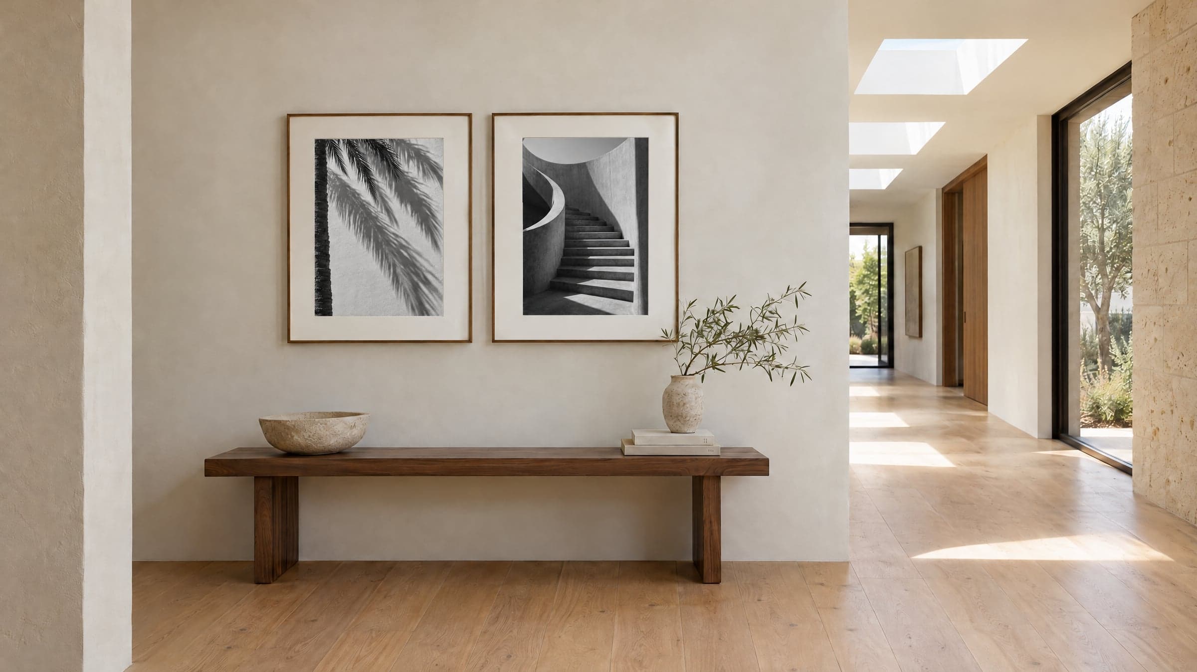 Two framed black and white prints above a wooden bench in a sunlit hallway