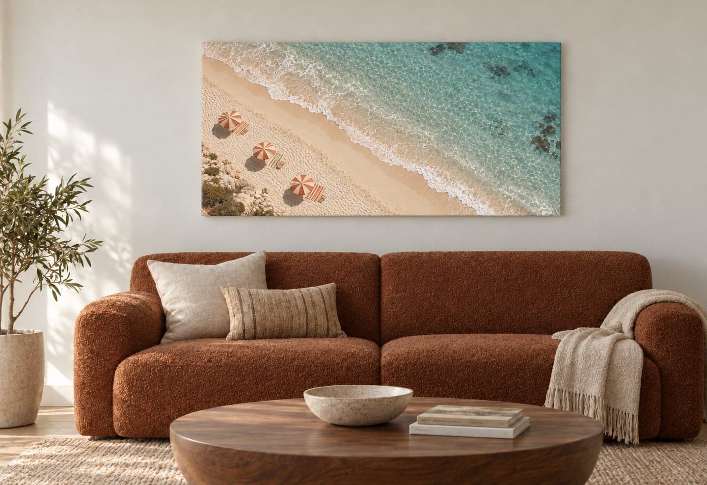 A canvas of a beach seen from above, umbrellas on the sand and turquoise water, above a rust sofa