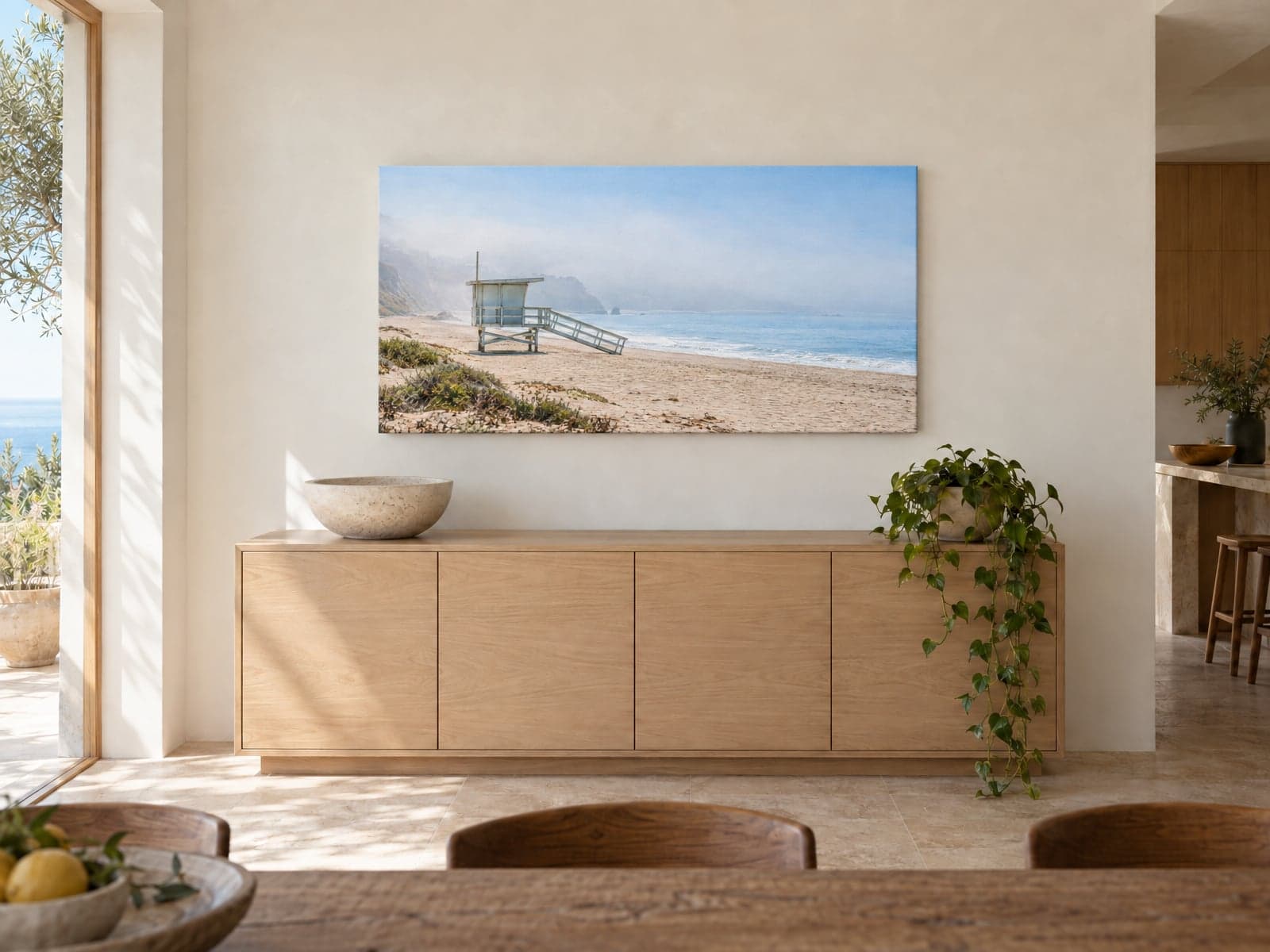 A wide canvas of a lifeguard tower on a misty beach above an oak sideboard